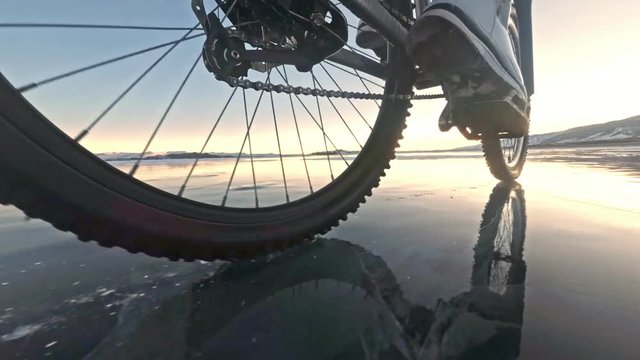 View of the tire. Shooting 60fps actioncam. Woman is riding bicycle on the ice. Ice of the frozen Lake Baikal. The tires on the bicycle are covered with special spikes. The traveler is ride a cycle.