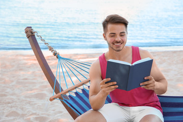 Obraz premium Young man reading book in hammock at seaside