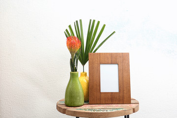 Blank frame and beautiful plants on table near white wall. Mock up for design