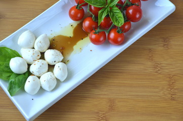 Italian Caprese salad. Close up of mozzarella cheese and cherry tomato salad with balsamic vinegar, olive oil and basil top view
