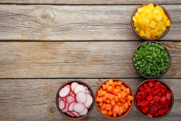 Fresh sliced vegetables in bowls on wooden table