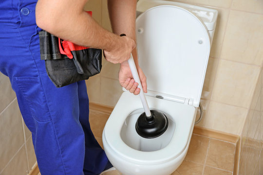 Plumber repairing toilet with hand plunger indoors