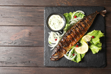 Slate plate with delicious grilled fish and sauce on wooden table, top view