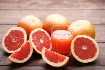 Ripe grapefruits and glass of juice on brown wooden table