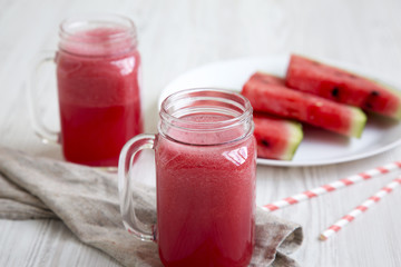 Watermelon smoothie in glass jars with fresh slices of water melon over white wooden surface, side view. Closeup.