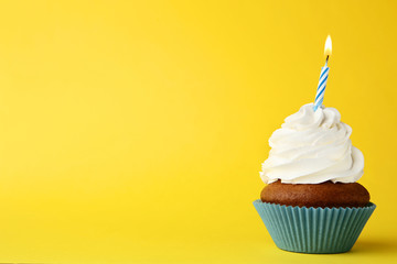 Tasty cupcake with candle on yellow background