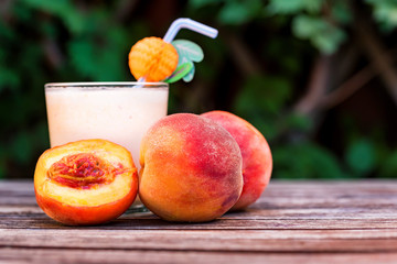 Glass of peach yoghurt and peaches on wooden table