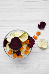 Full bowl of veggie chips on white wooden background, view from above. Closeup.