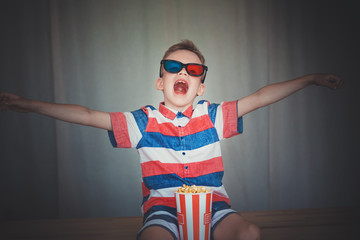 Naklejka premium Young boy watch a movie in 3D glasses at the cinema or at home. Little kid eat popcorn over gray background. Home theater. Cute Child in vintage cinema eyeglasses