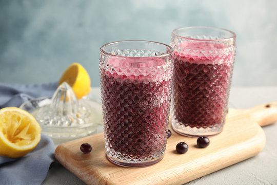 Glasses of delicious acai juice on table against color background