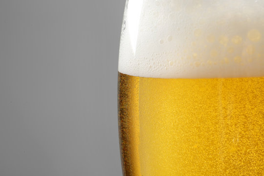 Glass of tasty beer with foam on color background, closeup