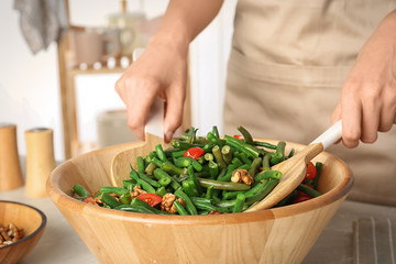 Woman preparing healthy salad with green beans, cherry tomatoes and walnuts at table