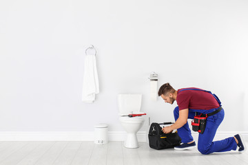 Young man with tool kit bag near toilet bowl in bathroom