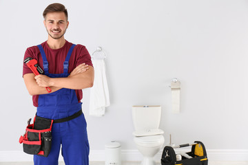 Young man with plumber wrench and toilet bowl on background - obrazy, fototapety, plakaty