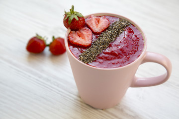 Pink cup of strawberry smoothie with chia seeds on white wooden table, side view. Closeup.