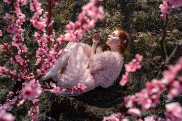 Beautiful young girl with red hair in a gentle peach garden, which blossomed.