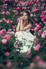 Beautiful woman in a floral park, garden roses. Makeup, hair, a wreath of roses.
