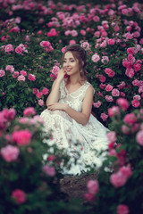 Beautiful woman in a floral park, garden roses. Makeup, hair, a wreath of roses.