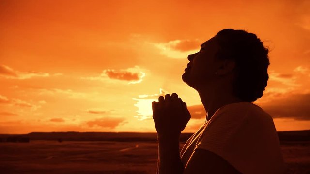 the girl prays. Girl folded her hands in prayer lifestyle silhouette at sunset. slow motion video. Girl folded her hands in prayer pray to God. girl praying asks forgiveness for sins of repentance
