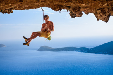 Male climber on overhanging rock arch, beautiful view of coast below.