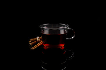Cup of Tea and Cinnamon Sticks on a reflective surface, isolated on black background