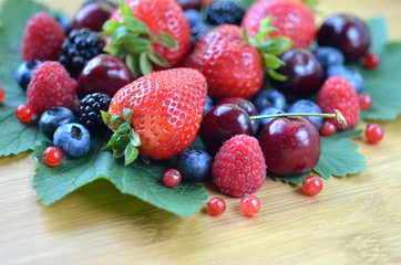 Detail of fresh summer fruit and berries on a bamboo board. Strawberries, raspberries, cherries, blackberries, blueberries and red currants on fresh green leaves with copy space.

