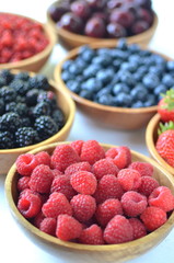 Detail of fresh summer fruit and berries in wooden bowls. Strawberries, raspberries, cherries, blackberries, blueberries and red currants top view.
