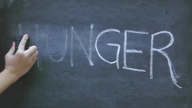 Erasing the word hunger written in white chalk on a black chalkboard