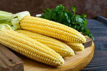 Young corn cobs with leaves, spices, herbs, sea salt on a wooden tray.