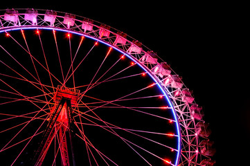 Big ferris wheel with festive red illumination against night sky.