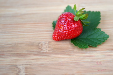 Detail of fresh summer fruit and berries on a bamboo board. Strawberries on fresh green leaves with copy space.
