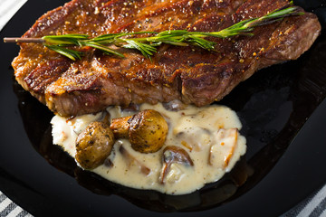 Beef steak with mushrooms sauce branch of rosemary at black plate