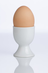 Brown egg in white porcelain cup, partial silhouette in foreground. 