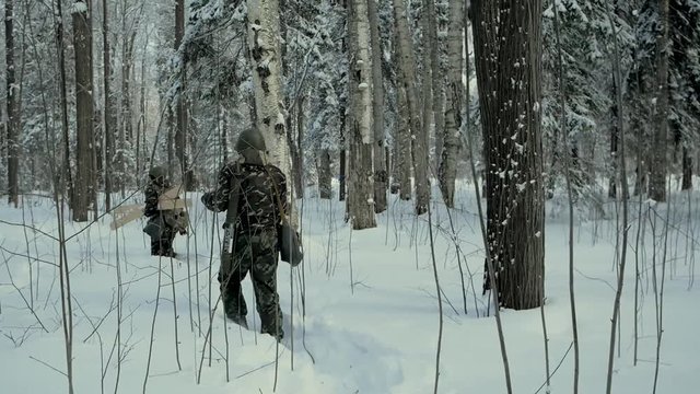 Group of soldiers run on skis in the woods with weapons. Clip. Soldiers with AK-47 rifles and grenade launchers running through the winter forest on skis. Soldiers on exercises in the woods in winter
