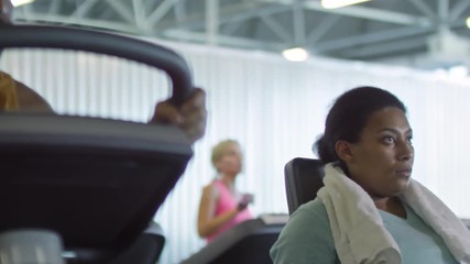 PAN of focused Arab man and black woman training on stationary bikes in gym