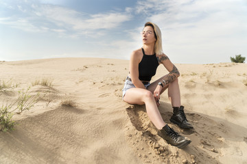 Portrait of a woman in shorts sitting on the sand in the desert and looking sideways