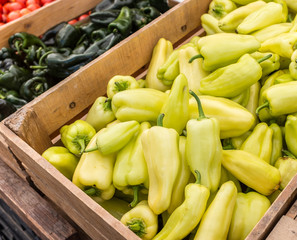 Wooden bins of yellow and green peppers at a farmers market.