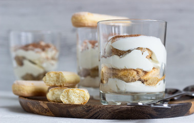 Traditional Italian dessert tiramisu in glass on light grey background. Coffee flavored Italian dessert made of ladyfingers and mascarpone. 