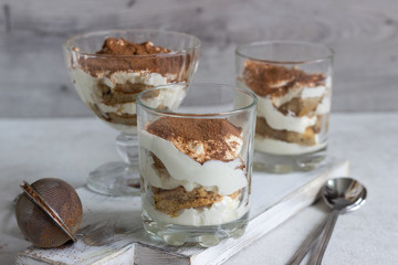 Traditional Italian dessert tiramisu in glass on light grey background. Coffee flavored Italian dessert made of ladyfingers and mascarpone. 