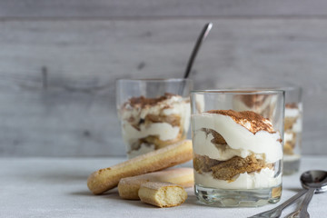 Traditional Italian dessert tiramisu in glass on light grey background. Coffee flavored Italian dessert made of ladyfingers and mascarpone. 