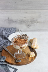 Traditional Italian dessert tiramisu in glass on light grey background. Coffee flavored Italian dessert made of ladyfingers and mascarpone. 