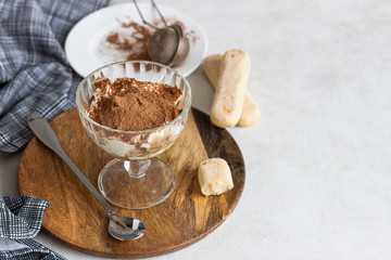 Traditional Italian dessert tiramisu in glass on light grey background. Coffee flavored Italian dessert made of ladyfingers and mascarpone. 