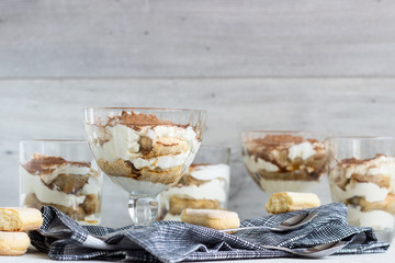 Traditional Italian dessert tiramisu in glass on light grey background. Coffee flavored Italian dessert made of ladyfingers and mascarpone. 