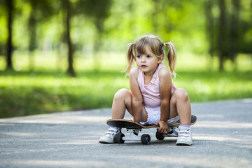 Little blonde girl playing with skateboard in forest park
