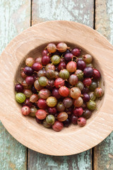 Organic berries. Ripe pink gooseberries in oak plate on shabby blue wooden background copyspace