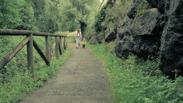4 k slow-motion beautiful young family, mother and son walking along the picturesque scenic contryside peatonal road at the green fairy tale forest
