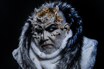 Dark arts concept. Senior man with white beard dressed like monster. Demon on black background, close up. Man with thorns or warts in fur coat. Alien, demon, sorcerer makeup.