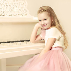 A little girl is sitting at the white piano.