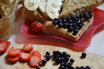Plate of sandwiches with peanut butter, jam and fresh fruits on white wooden background from top view