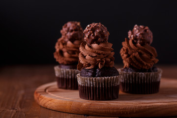 Tasty chocolate cupcakes on wooden board. Dark background